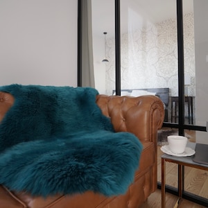 May include: A tan leather tufted sofa featuring a deep teal faux fur throw blanket draped over the seat. The sofa has a classic button-tufted back and rolled arms, providing a textured contrast against the smooth, polished surface of the leather.