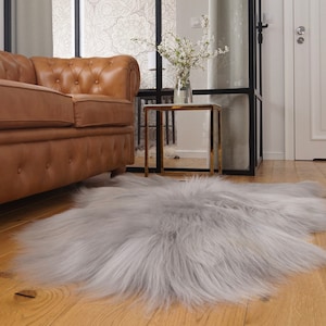 Puede incluir: Una alfombra de piel de oveja gris claro con pelo largo y esponjoso, colocada sobre un suelo de madera en un salón.