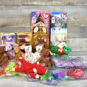 May include: A collection of Ty Beanie Babies, including Britannia the Bear, Maple the Bear, and other plush toys. The toys are in their original packaging and are in excellent condition.