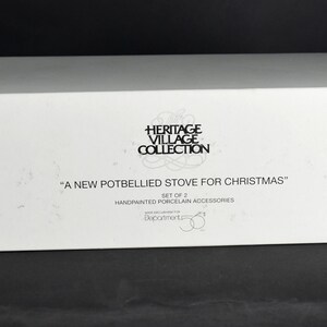 Puede incluir: Caja blanca con texto negro que dice "Heritage Village Collection" y "A New Potbellied Stove for Christmas". La caja tambi&eacute;n dice "Set of 2 Handpainted Porcelain Accessories".