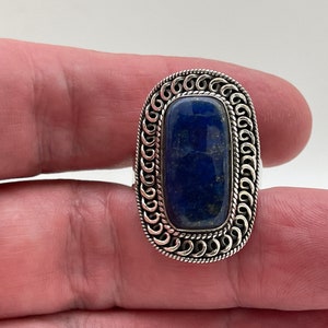 May include: A silver ring with a dark blue lapis lazuli stone set in a decorative, ornate silver bezel.