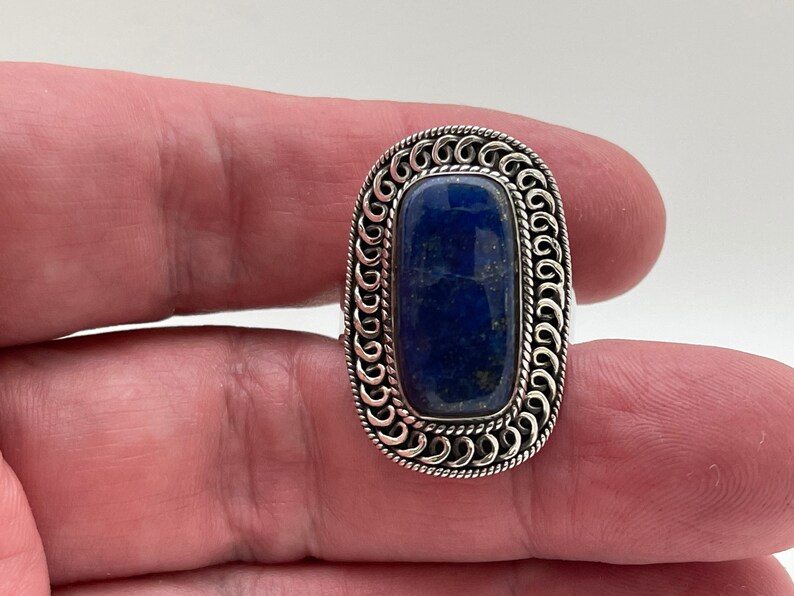 May include: A silver ring with a dark blue lapis lazuli stone set in a decorative, ornate silver bezel.