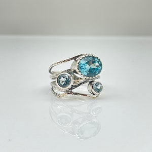 May include: A silver ring with three blue topaz gemstones. The ring has a delicate, twisted design.