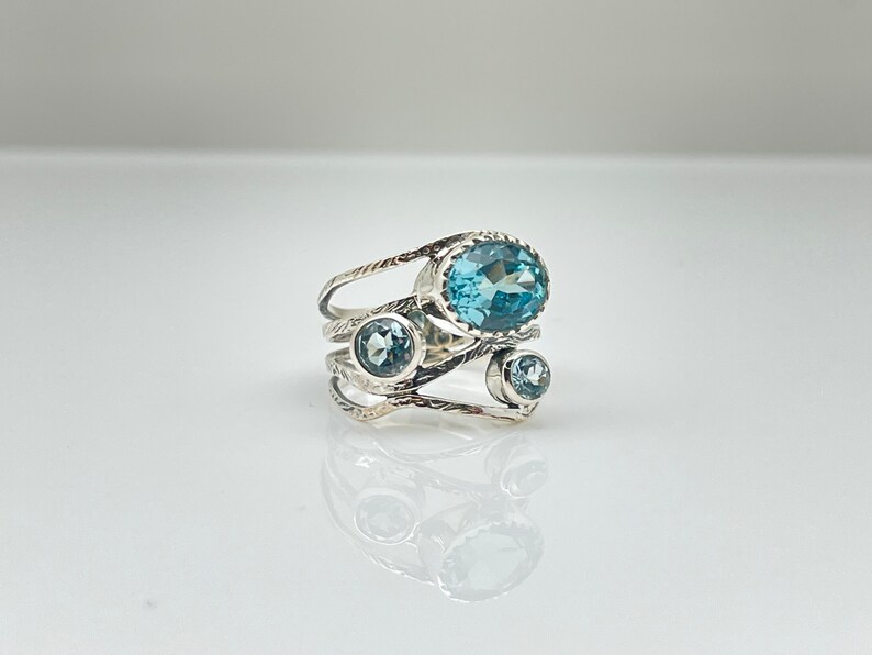 May include: A silver ring with three blue topaz gemstones. The ring has a delicate, twisted design.