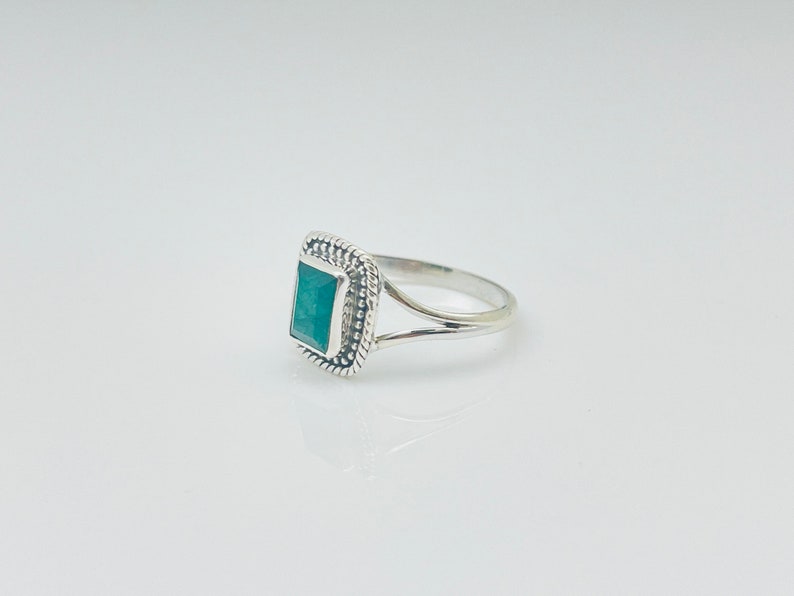 Puede incluir: Un anillo de plata con una piedra preciosa verde cuadrada engastada en un borde de cuentas.