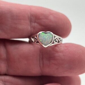 May include: A silver ring with a heart-shaped opal gemstone. The ring has a delicate, ornate design.