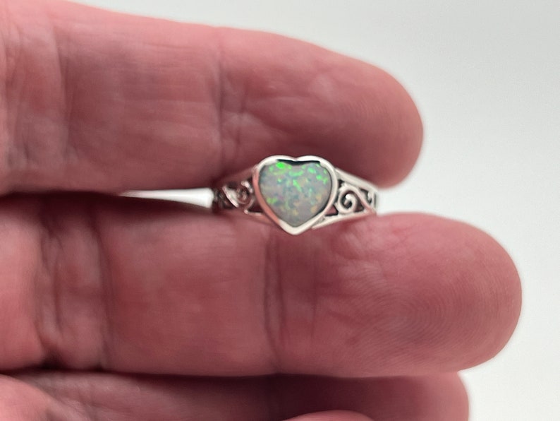 May include: A silver ring with a heart-shaped opal gemstone. The ring has a delicate, ornate design.