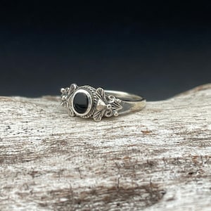 May include: A silver ring with a black oval gemstone set in a floral design.