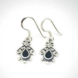 May include: A pair of silver dangle earrings with black teardrop-shaped stones. The earrings have a delicate, ornate design.