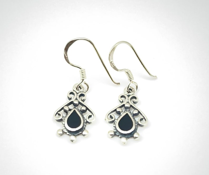 May include: A pair of silver dangle earrings with black teardrop-shaped stones. The earrings have a delicate, ornate design.