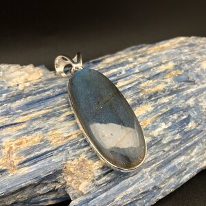 May include: A silver pendant featuring a large oval-shaped labradorite gemstone with iridescent blue and green hues.