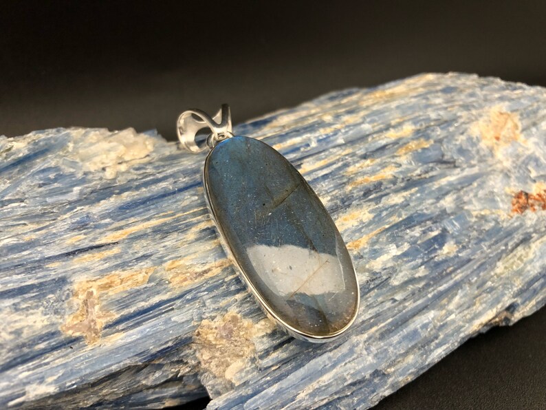 May include: A silver pendant featuring a large oval-shaped labradorite gemstone with iridescent blue and green hues.