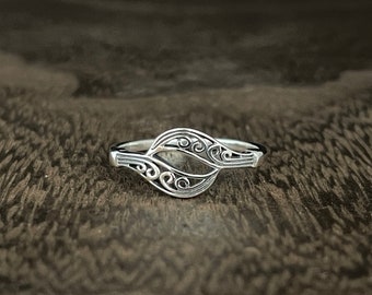 May include: A silver ring with a delicate, intricate design featuring swirling patterns. The ring is open and has a wide band.