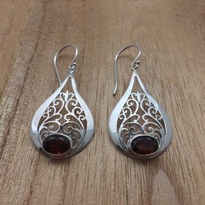 Puede incluir: Un par de pendientes de filigrana de plata con acentos de piedras preciosas rojas. Los pendientes tienen forma de l&aacute;grima y presentan intrincados dise&ntilde;os florales.