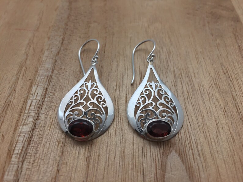 Puede incluir: Un par de pendientes de filigrana de plata con acentos de piedras preciosas rojas. Los pendientes tienen forma de l&aacute;grima y presentan intrincados dise&ntilde;os florales.