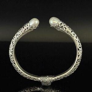 May include: Silver-toned cuff bracelet with ornate, swirling filigree design. The bracelet features a pearl at each end. The open design allows for easy wear. A beautiful piece of jewelry.