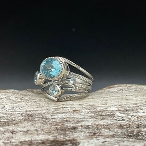 May include: A silver ring with three blue topaz gemstones set in a delicate, multi-layered band.