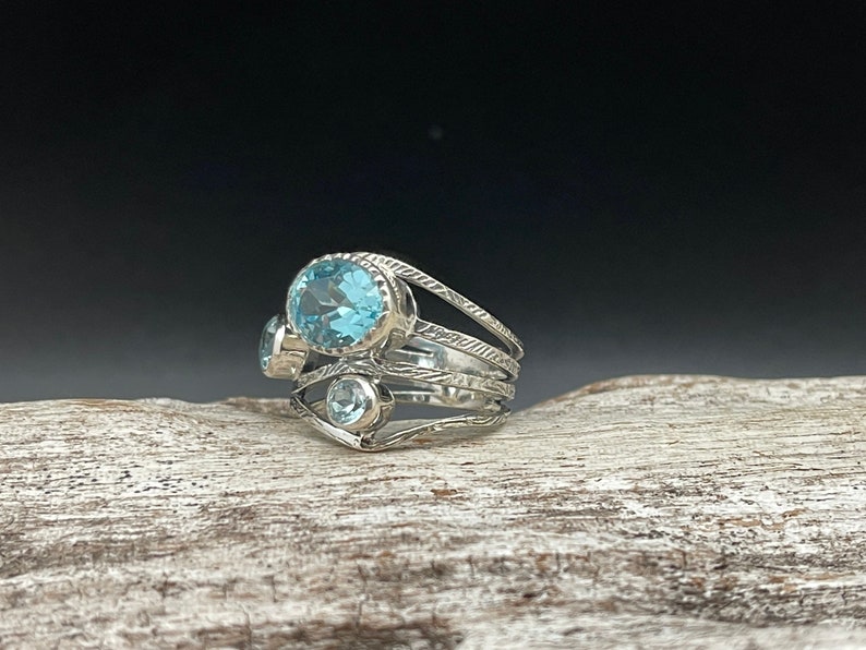 May include: A silver ring with three blue topaz gemstones set in a delicate, multi-layered band.