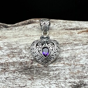 May include: A silver heart-shaped pendant with an intricate design and a purple amethyst gemstone in the center.