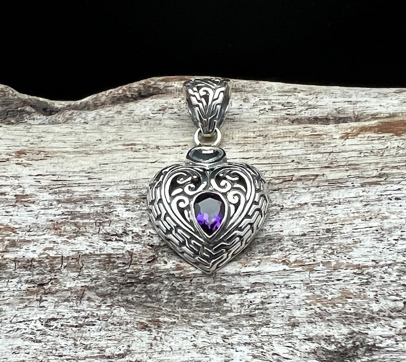 May include: A silver heart-shaped pendant with an intricate design and a purple amethyst gemstone in the center.