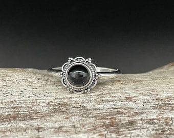 May include: A silver ring featuring a black gemstone set within an ornate floral design.
