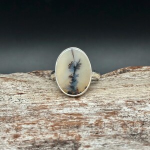 K&ouml;nnte beinhalten: Ovaler Silberring mit einem Dendritachat-Stein. Der Stein zeigt schwarze und blaue Einschl&uuml;sse auf cremewei&szlig;em Grund. Der Ring ist auf einem strukturierten Silberband gefasst. Ein einzigartiges, handgefertigtes Schmuckst&uuml;ck.