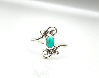 May include: A sterling silver ring featuring an oval turquoise stone. The ring has a decorative, swirling design on either side of the stone. The turquoise stone is a vibrant blue-green color. The ring is set against a white background.