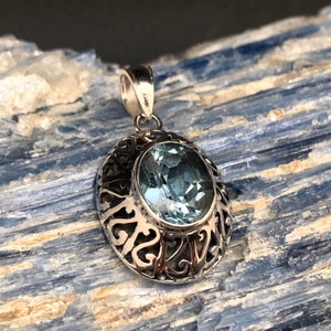 May include: A silver pendant with an oval-shaped blue topaz gemstone set in a filigree design.