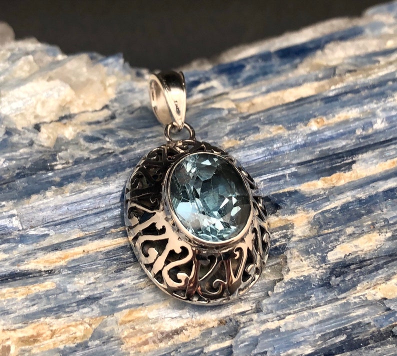 May include: A silver pendant with an oval-shaped blue topaz gemstone set in a filigree design.