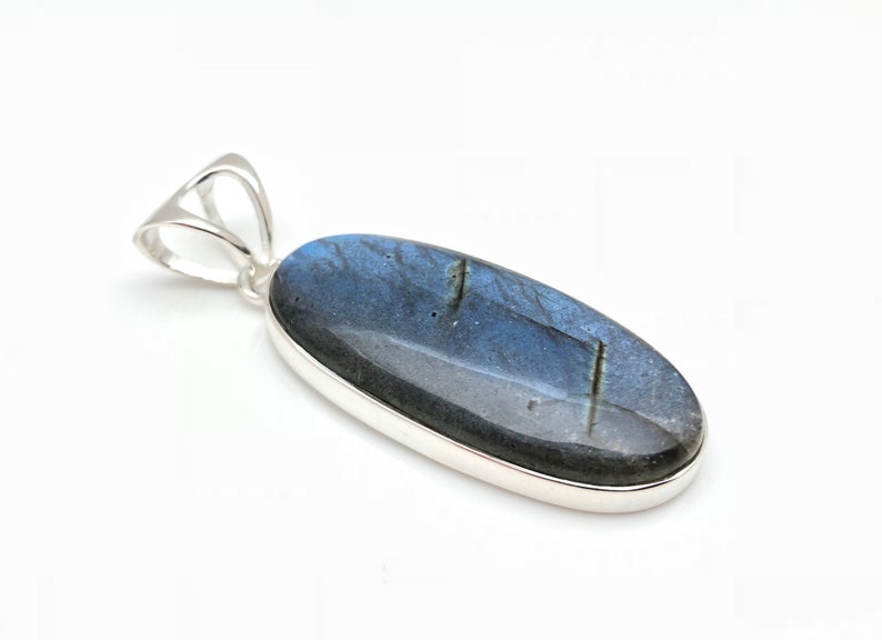 May include: A silver pendant featuring a large oval-shaped labradorite gemstone with blue and black iridescent hues.