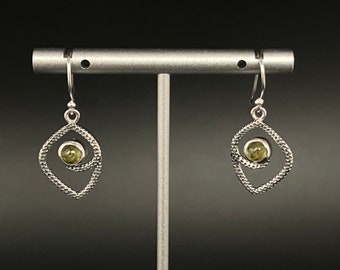 May include: A pair of silver dangle earrings with a green gemstone in the center of each earring. The earrings are in the shape of a diamond with a smaller diamond shape inside.