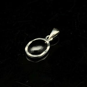 Puede incluir: Un colgante de plata con una piedra preciosa negra ovalada. El colgante tiene un dise&ntilde;o sencillo y elegante con un borde de plata martillada. La argolla es un peque&ntilde;o lazo para una cadena.