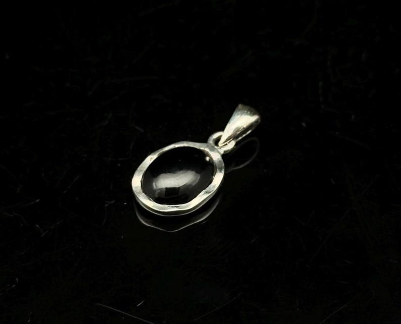 Puede incluir: Un colgante de plata con una piedra preciosa negra ovalada. El colgante tiene un dise&ntilde;o sencillo y elegante con un borde de plata martillada. La argolla es un peque&ntilde;o lazo para una cadena.