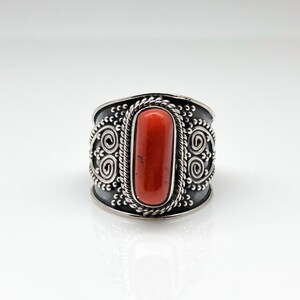May include: A silver ring with an orange stone set in a decorative band. The band is adorned with intricate swirls and dots.