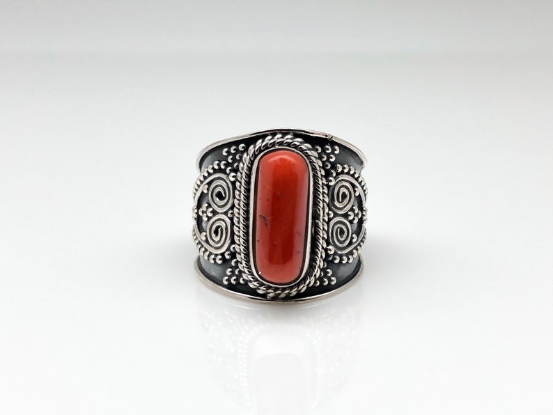 May include: A silver ring with an orange stone set in a decorative band. The band is adorned with intricate swirls and dots.