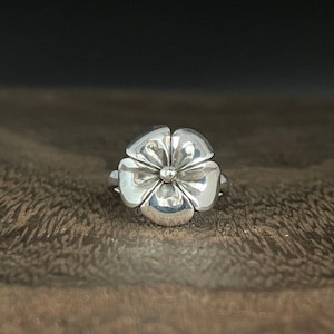 May include: A silver ring with a flower design. The flower has five petals and a small center bead.