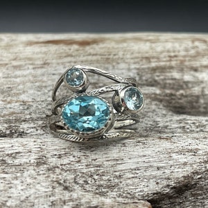 May include: A silver ring with three blue topaz gemstones set in a twisted band.