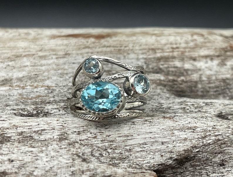 May include: A silver ring with three blue topaz gemstones set in a twisted band.
