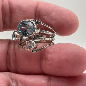 May include: A silver ring with three blue topaz gemstones. The ring has a delicate, intricate design with multiple bands.