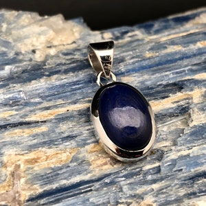 May include: A silver pendant with a dark blue oval gemstone set in a silver bezel.