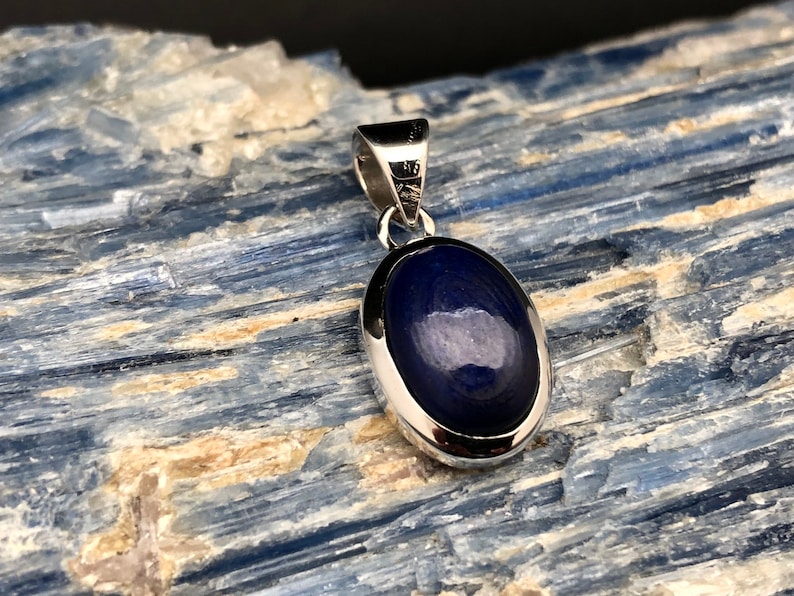 May include: A silver pendant with a dark blue oval gemstone set in a silver bezel.
