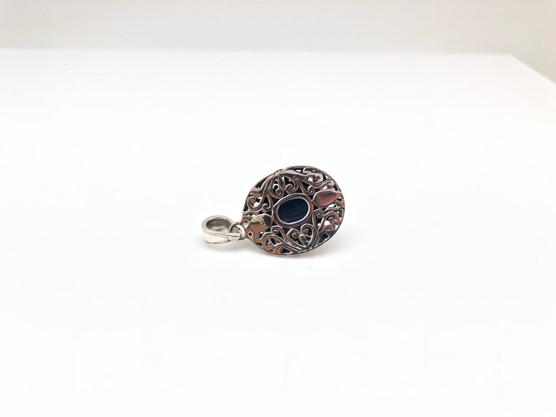 May include: Silver pendant with an oval black stone set in a filigree design.