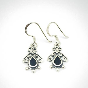 May include: A pair of silver dangle earrings with black teardrop-shaped stones set in a filigree design.