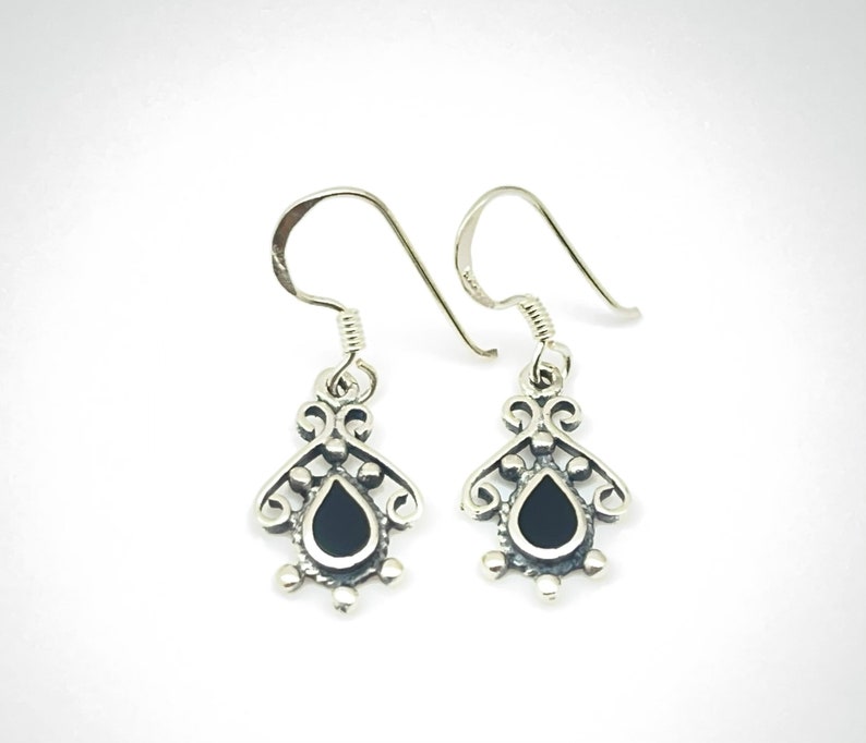 May include: A pair of silver dangle earrings with black teardrop-shaped stones set in a filigree design.
