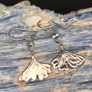 May include: Silver earrings with a ginkgo leaf design and a light blue gemstone dangle.