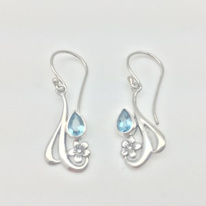 May include: Sterling silver earrings featuring a delicate floral design and a teardrop-shaped blue topaz gemstone.