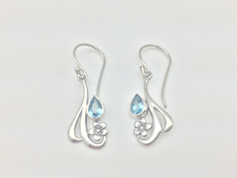 May include: Sterling silver earrings featuring a delicate floral design and a teardrop-shaped blue topaz gemstone.