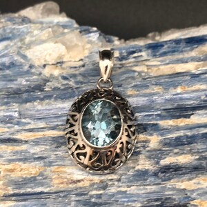 May include: A silver pendant with an oval-shaped blue topaz gemstone set in a filigree design.