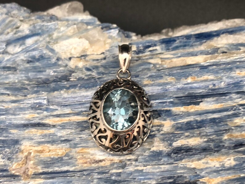 May include: A silver pendant with an oval-shaped blue topaz gemstone set in a filigree design.