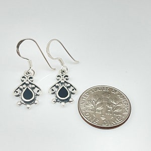 May include: A pair of silver dangle earrings with black teardrop-shaped stones. The earrings are about the size of a dime.